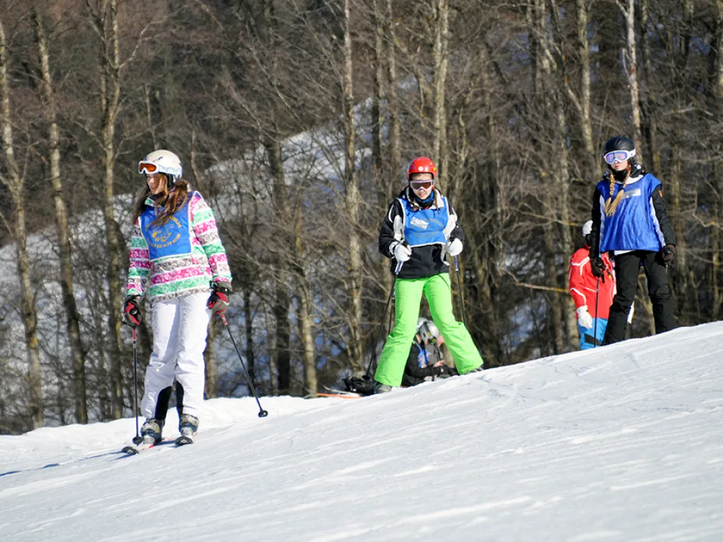 Zwei Skifahrerinnen auf der Piste am Waldrand.